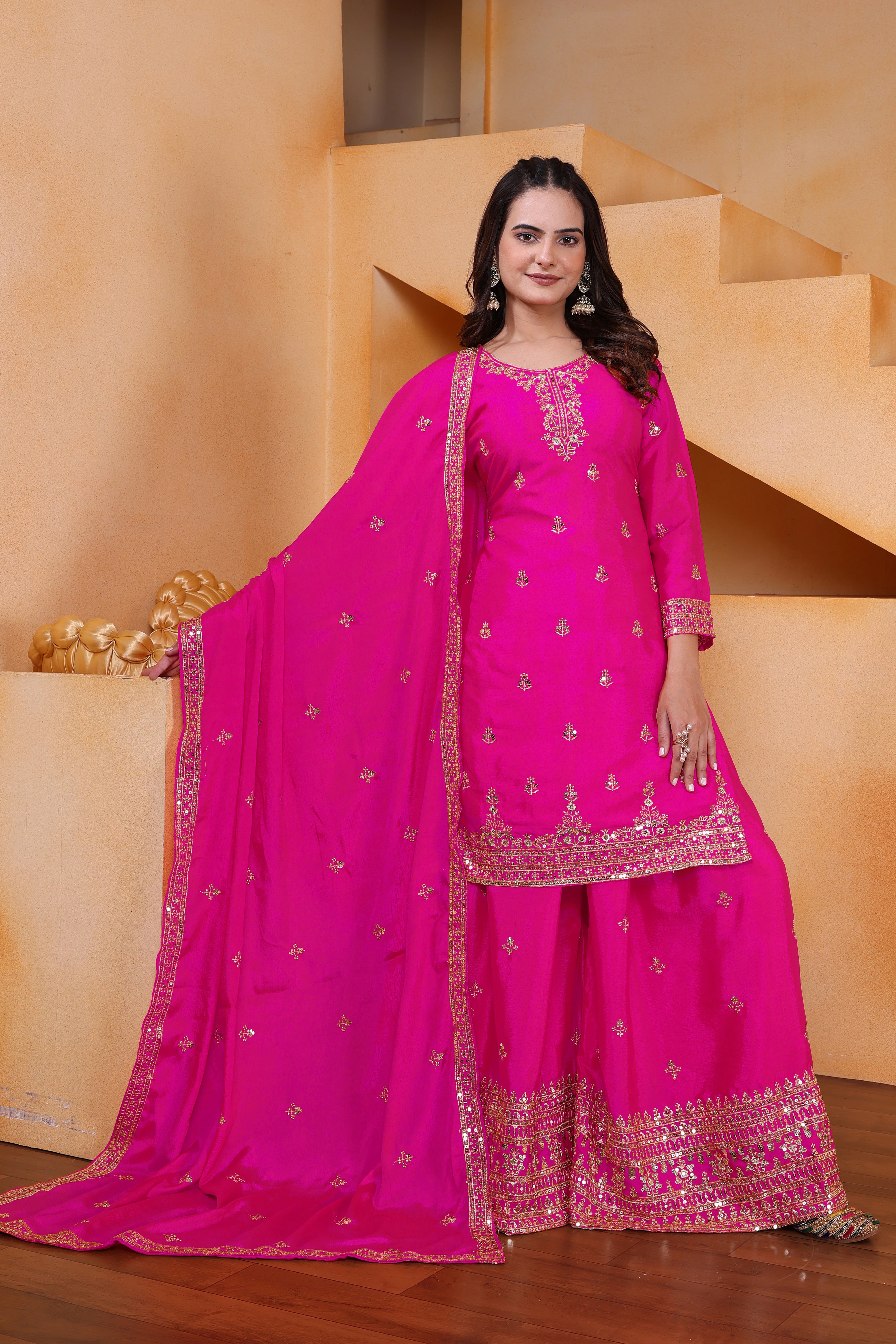 Woman in a bright pink traditional outfit with intricate designs standing in front of a staircase.